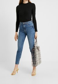 Top negro de manga larga, jeans ajustados de cintura alta en azul, tacones amarillos con tiras y un bolso de mano transparente a rayas.