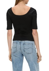 Svart åtsittande topp med bred båtringning och korta ärmar, kombinerad med bleka blå denimjeans med en klassisk femfickdesign.