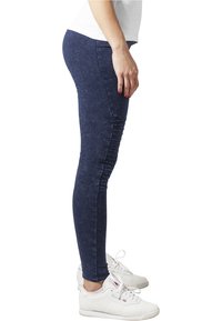 Marinblå leggings i stretchmaterial med ribbade detaljer längs sidan, kombinerat med vita sportskor.