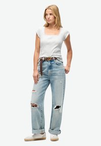 Camiseta gris ajustada con mangas acampanadas, combinada con unos vaqueros rectos de azul claro desgastados con múltiples desgastes. Cinturón marrón y zapatillas blancas.