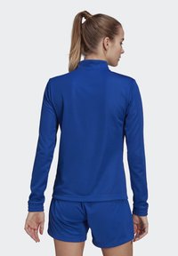 Camiseta atlética de manga larga en tejido azul liso, con cuello alto y diseño ajustado, combinada con pantalones cortos a juego. Textura suave, sin patrones.