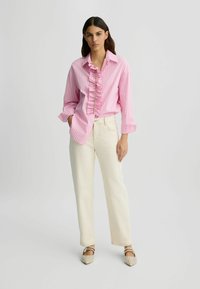 Chemisier à rayures roses et blanches avec un devant froncé et des détails de boutons, associé à un pantalon ample couleur crème et des chaussures ornées.