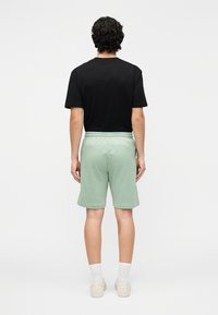 Čierna krátka košeľa s krátkymi rukávmi a svetlozelené šortky s elastickým pásom. Model má na sebe biele ponožky a svetlé topánky. Jednoduché pozadie.