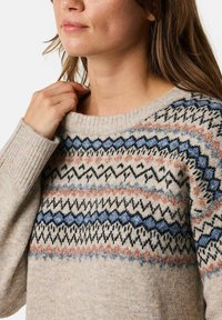 Lichtbeige trui met een geribde kraag. Voorzien van veelkleurige geometrische patronen in zwart, blauw en rozenkleuren. Zacht, textuurstof.