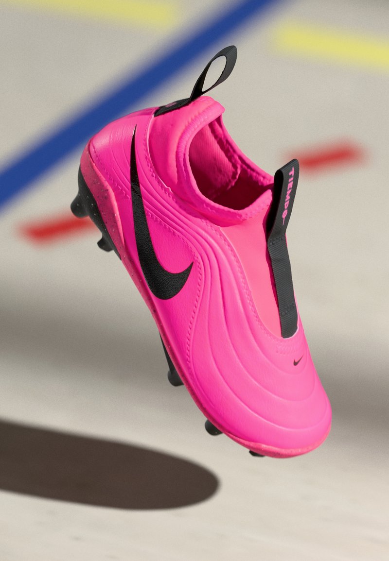 Botte de football rose avec un dessus texturé, logo Nike noir, et une étiquette en boucle noire. Semelle à crampons conçue pour l'adhérence sur les surfaces en herbe.