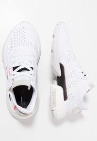 Zapatillas deportivas blancas con parte superior de malla, suela texturizada y acentos grises en contraste. Presenta cordones y soporte para el talón con la marca visible.