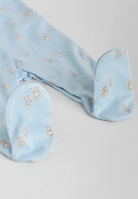 Pijamale albastru deschis cu imprimeu de ursuleț dintr-un material moale. Include închideri cu capse și forme rotunjite la picioare pentru confort.