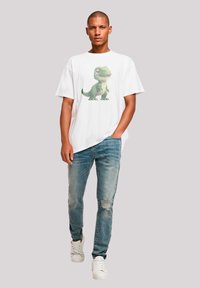 White cotton t-shirt featuring a green cartoon dinosaur print, paired with light blue distressed denim jeans and white sneakers.