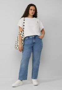 Jean droit bleu clair, t-shirt blanc, et baskets blanches. Le t-shirt présente un petit détail brodé. Un sac fourre-tout à pois est porté sur l'épaule.