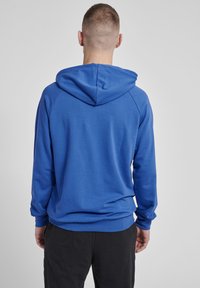 Sweat-shirt à capuche bleu avec des manches longues, en tissu doux, avec une poche kangourou et des poignets côtelés, présenté de dos.
