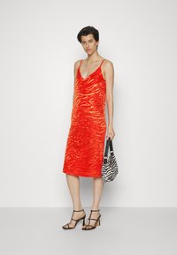 Vestido midi vermelho com um design texturizado que se assemelha a ondas, apresentando alças finas tipo spaghetti e um decote em V. Combinando com uma mala com padrão de zebra.