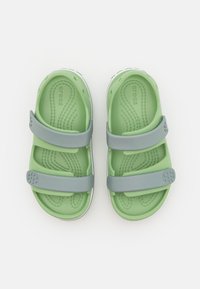 Vihreät Crocs-sandaalit, joissa on kaksi harmaata säädettävää hihnaa, teksturoitu sisäpohja ja valkoinen pohja, joissa on ilmanvaihtoaukkoja ja pyöreä logo.