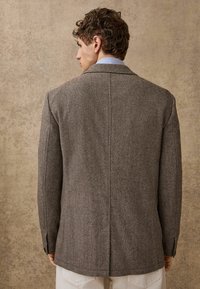 Brown herringbone blazer with a tailored fit, notched lapels, and single vent. Fabric texture is woven with a subtle pattern.