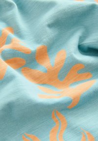 Türkiser Stoff mit einem orangefarbenen korallenartigen Muster, das eine weiche Textur und einen geschmeidigen Fall aufweist und abstrakte Formen sowie fließende Linien betont.