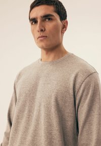 Szary sweatshirt z okrągłym dekoltem wykonany z miękkiej bawełny, charakteryzujący się luźnym krojem i subtelną teksturą, o minimalistycznym wzornictwie.