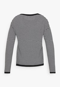 Black and white checkered long-sleeve sweater with a rounded neckline and contrasting black cuffs at the hem and sleeves.