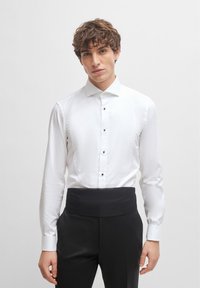 White dress shirt with a classic collar, featuring a placket of black buttons and a smooth texture, paired with pleated black trousers.