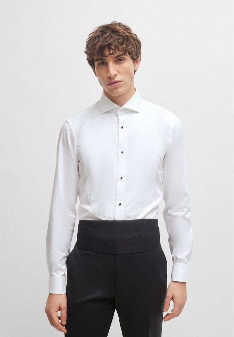 White dress shirt with a classic collar, featuring a placket of black buttons and a smooth texture, paired with pleated black trousers.