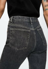 Černé džíny z denimu s vysokým pasem, s klasickým designem zadní kapsy a jemnými detaily šití. Hladká textura a přiléhavý střih.