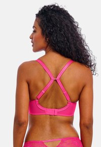 Soutien-gorge rose au design sportif avec des bretelles croisées dans le dos, des clips ajustables et une texture lisse. Forme arrondie avec un minimum de détails.