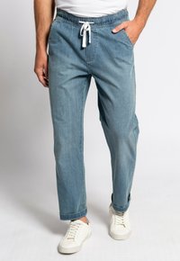 Pantalones jogger de mezclilla azul claro con cintura elástica y cordón, que cuentan con bolsillos laterales y un corte relajado, combinados con zapatillas blancas.