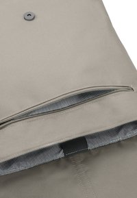 Beige tygväska med dragkedjestängning. Inuti finns ett randigt mönster. En silverknapp syns på utsidan. Texturerad yta.