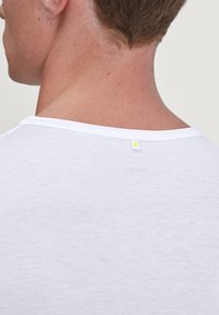 White T-shirt displays a soft, textured fabric. Crew neck design features a small yellow tag on the back, near the neckline.