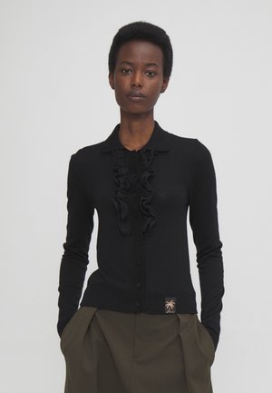 Schwarze Strickjacke mit Rüschendetail an der Vorderseite, mit Kragen und langen Ärmeln. Enthält ein Logoetikett mit einem Palmendesign.