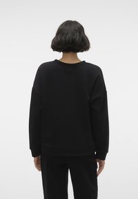 Sudadera negra de gran tamaño con cuello redondo, hombros caídos y puños acanalados. Textura suave, diseño minimalista.