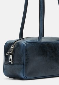 Un sac à main en cuir texturé bleu foncé avec double poignées, fermetures éclair argentées et un subtil marquage de la marque sur le devant.