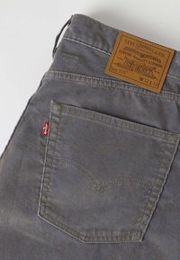 Γκρι τζιν Levi's με ορατή πίσω τσέπη, κόκκινη ετικέτα Levi's και καφέ δερμάτινο έμπλαστρο με λεπτομέρειες μάρκας και μεγέθους.