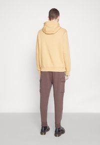 Senapsgul huvtröja med ribbad nederdel, kombinerad med bruna cargobyxor med sidofickor och vita detaljer, bärs med svarta kängor.