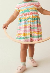 Robe multicolore en tissu ribbed avec des motifs en forme de vagues en rose, vert, jaune et bleu ; manches courtes ; bords de manches volantés ; portée avec des baskets roses.