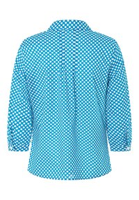 Chemise bleue à pois blancs, avec un col, un détail boutonné dans le dos et des manches trois-quarts avec option de roulage.