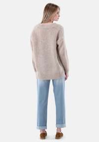 Beiger Strickpullover mit lockerer Passform, ausgestattet mit einem gerippten Halsausschnitt und Bündchen, kombiniert mit hellblauen, hochgekrempelten Jeans und braunen Slippern.