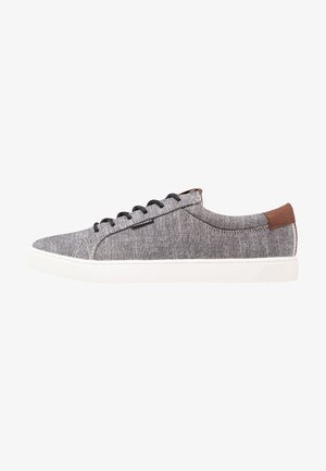 Basket basse décontractée avec tige en tissu gris, lacets noirs, semelle en caoutchouc blanche et accent en cuir marron au talon, vue de côté.