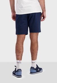 Mörkblå bomullsshorts med elastisk midja. Bärs med vita strumpor som har en logo och blå detaljer, tillsammans med mörkblå sneakers.