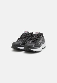 Sneakers atletici neri con tomaia testurizzata, suola bianca e dettagli di design curvi. Presentano lacci e un logo sulla linguetta.