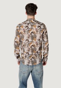 Camicia a maniche lunghe con stampa tropicale multicolore di foglie e scimmie, realizzata in tessuto leggero, abbinata a jeans blu slavati.