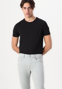 Tricou negru cu mânecă scurtă, asortat cu blugi slim-fit de culoare gri deschis. Tricoul are un guler rotund, iar blugii au buzunare frontale și închidere cu nasture.