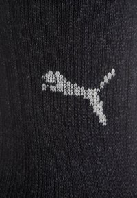 Czarna, dziana skarpetka z teksturowaną powierzchnią i wyraźnym, szarym logiem Pumy. Dostosowuje się do standardowego kształtu stopy dzięki elastycznemu mankietowi.