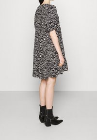 Robe à motifs noirs et blancs avec manches courtes, ourlet à volants superposés et coupe ample. Portée avec des bottines noires à talon bas.