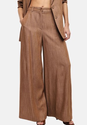 Pantaloni marroni a gamba larga con vita alta e chiusura con bottoni, abbinati a un blazer marrone coordinato e sandali con punta aperta.
