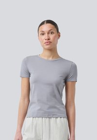 Grå kortærmet t-shirt lavet af blødt stof, med rund halsudskæring og tætsiddende design, båret sammen med stribede lyse bukser.
