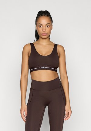 Brown sports bra with wide straps, scoop neckline, and an elastic band featuring white branding. Paired with matching high-waisted leggings.