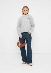 Pull léger gris clair avec un col en V et "A&Z" brodé. Jean en denim bleu foncé. Petit sac à main en croûte de cuir brun avec une bandoulière courte.