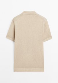 Beige polo tričko s krátkým rukávem, ribbovaným límcem a lemem. Měkká textura a bezešvé ramena zdůrazňují minimalistický design.