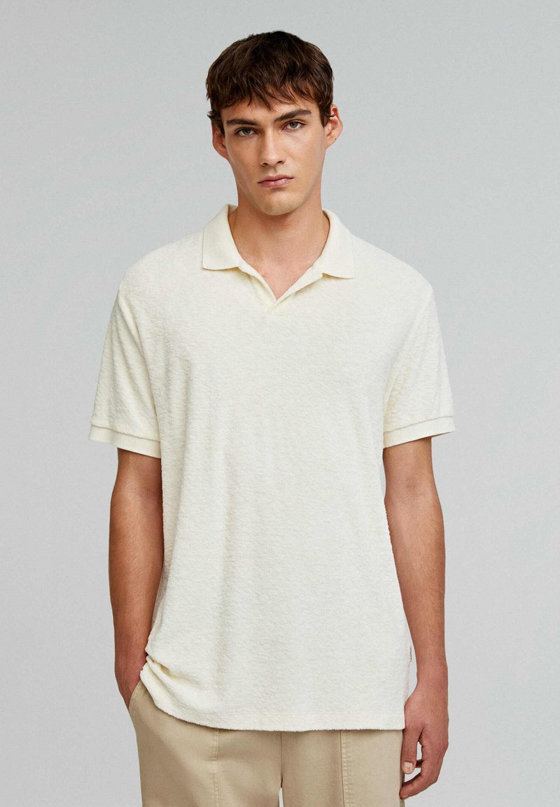 Crème-kleurige polo met korte mouwen en een textuur, een klassieke kraag en een relaxte pasvorm, gecombineerd met beige broek.
