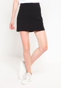 Svart minikjol med slät yta, med sidofickor och rak skärning, i kombination med vita sneakers.