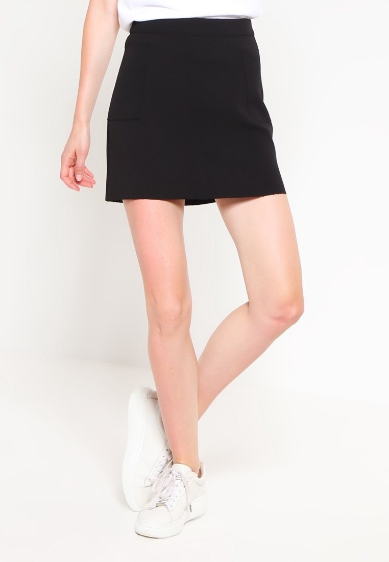 Svart minikjol med slät yta, med sidofickor och rak skärning, i kombination med vita sneakers.